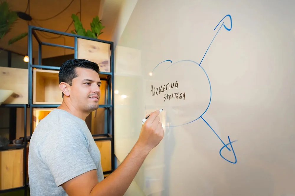 A man writing a marketing strategy on a whiteboard.
