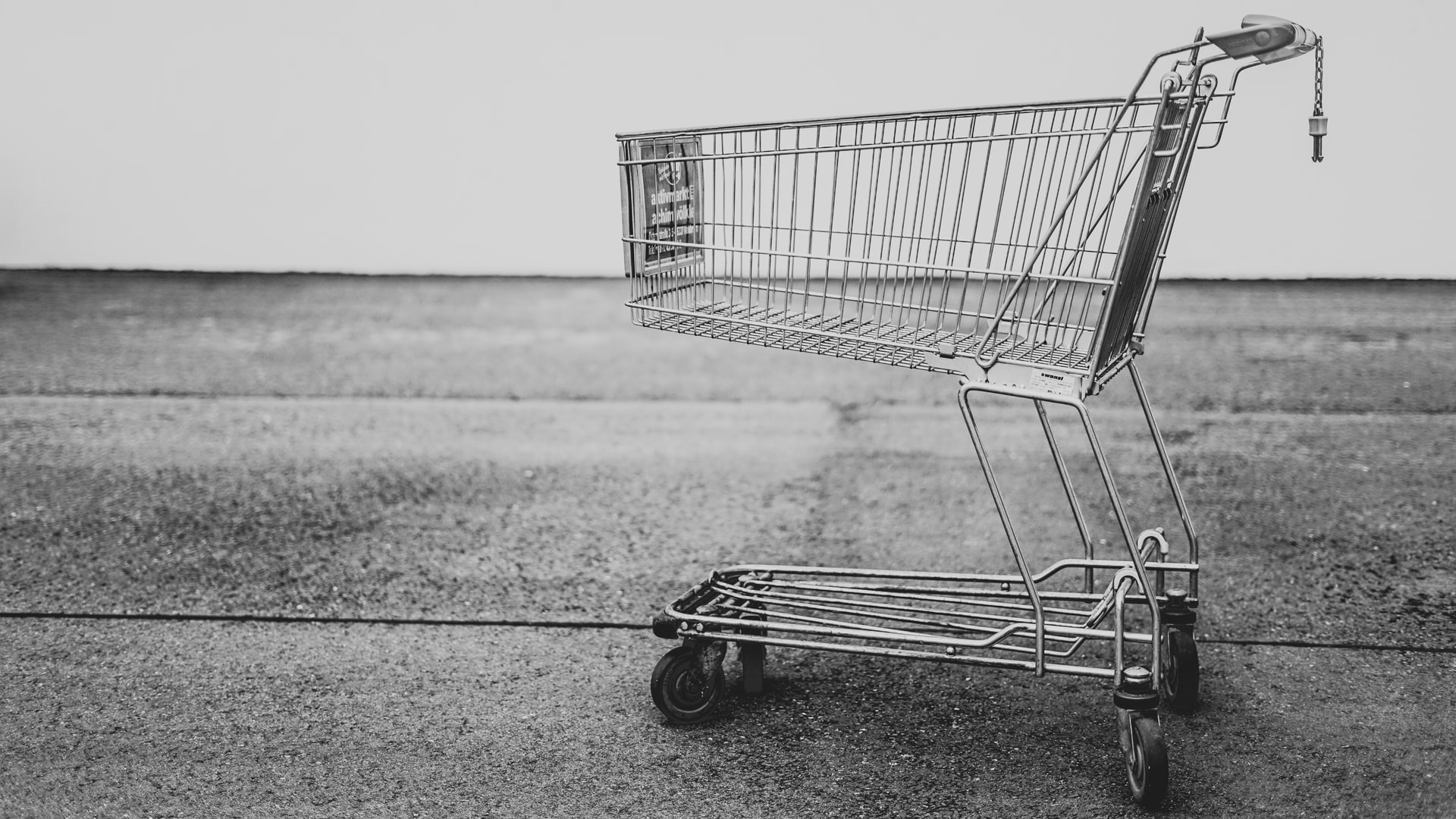 A grocery store cart on pavement, shown in black and white.