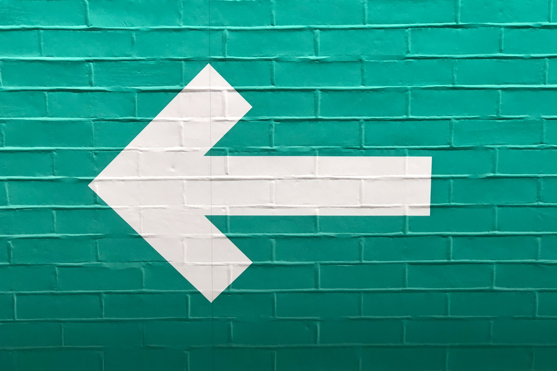 A white arrow on a green wall pointing left.