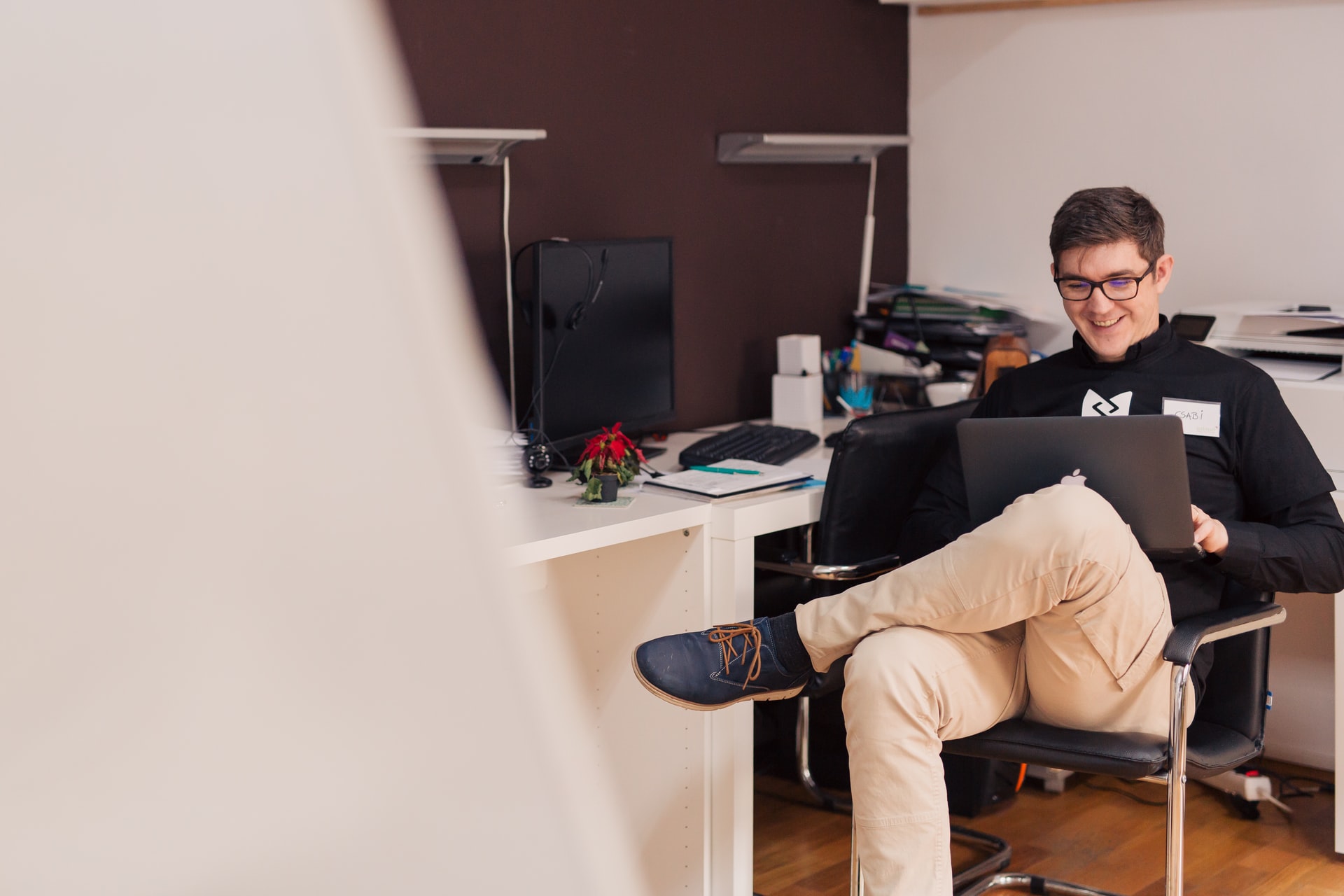 A person sits smiling down at their laptop while in their office.