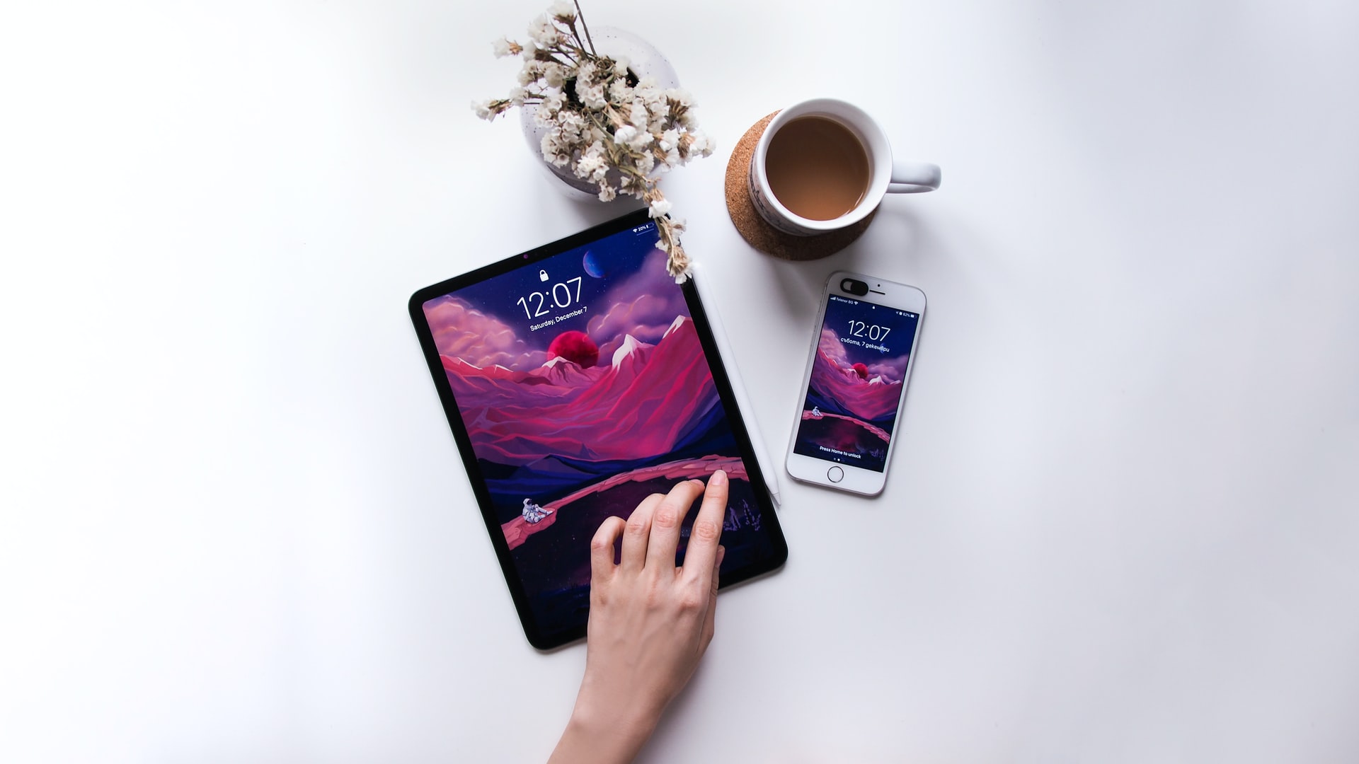 An iPad, iPhone, cup of coffee, and flowers sit on top of a white desk.