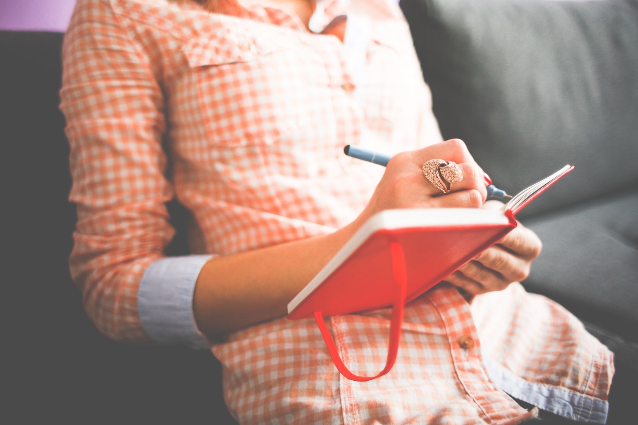 Person with a large ring on their hand writes in a red notebook.