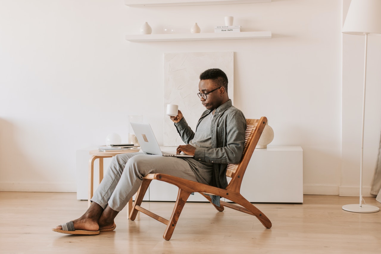 A person sips coffee while typing on a laptop.