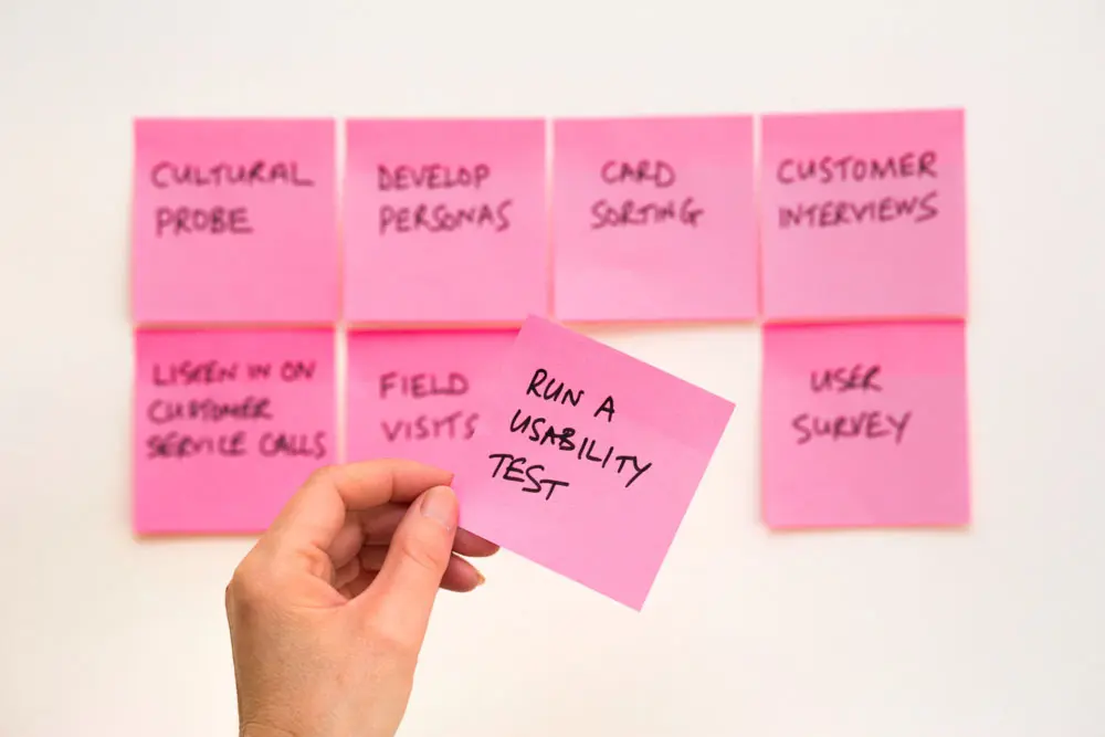 A person hands holding a sticky note that reads "Run A Usability Test".