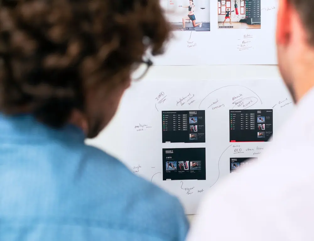 Two people looking at wireframe designs with notes on a white board.