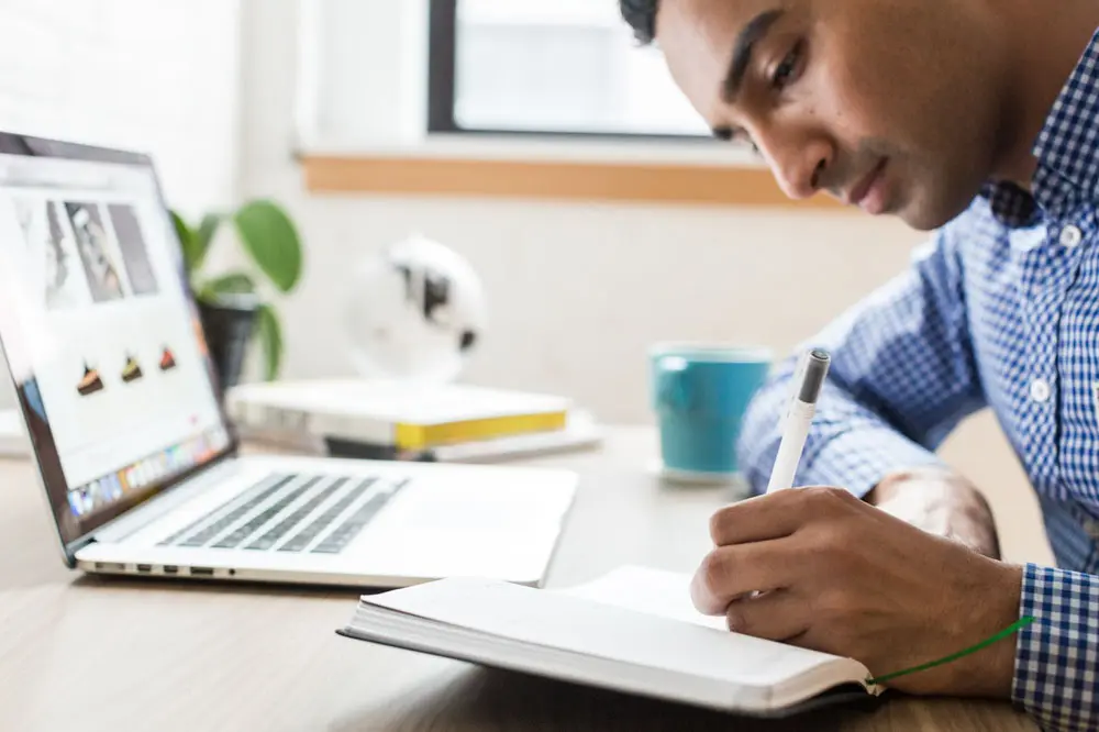 A person taking notes in front of their laptop for scaling up business goals.