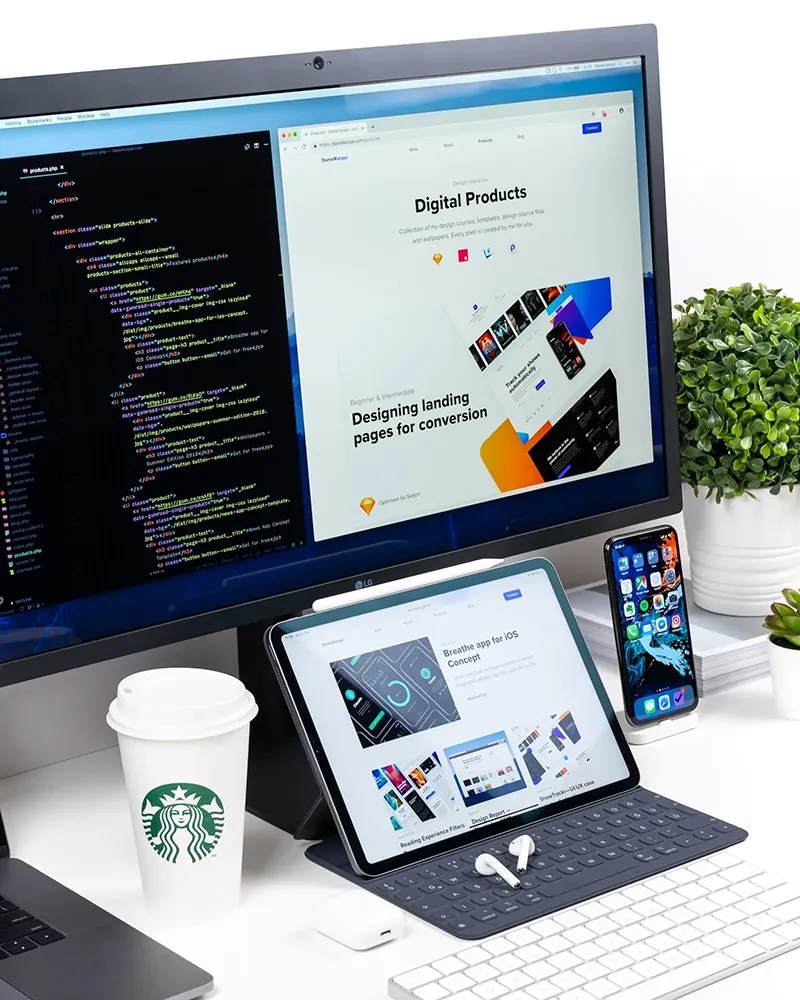 Three screens on a desk—a monitor with code, a laptop displaying a website, and an iPhone on the Home Screen.