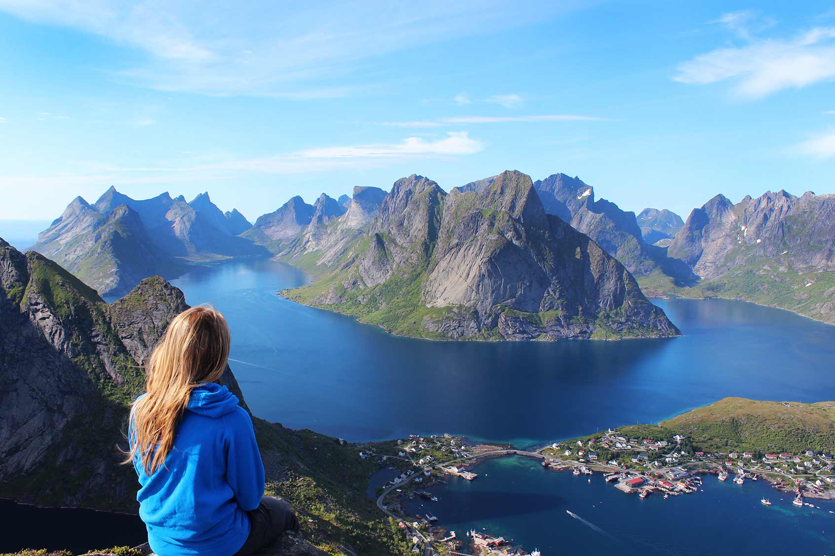 A person sitting on a cliff staring across towards large mountains.