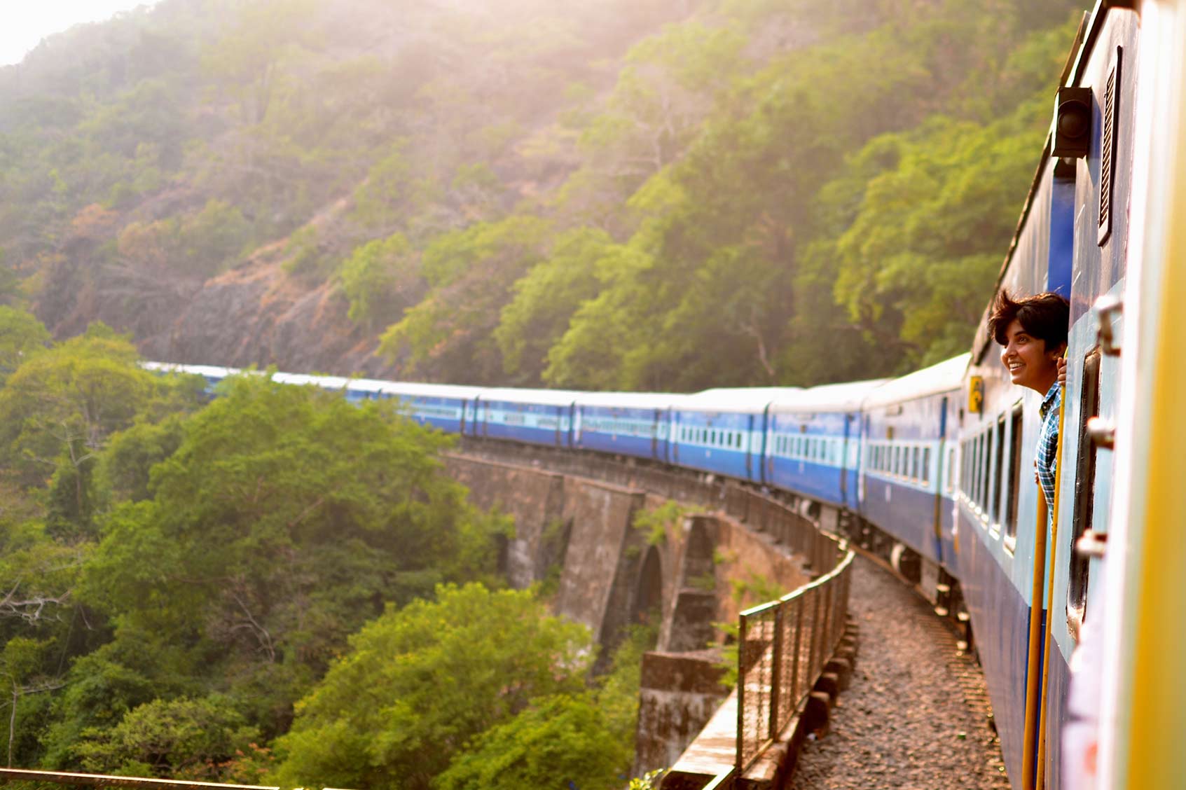 A person peeking their head out of a train and smiling while looking at the beautiful scenery.