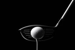 A golf club and a golf ball against a black backdrop.