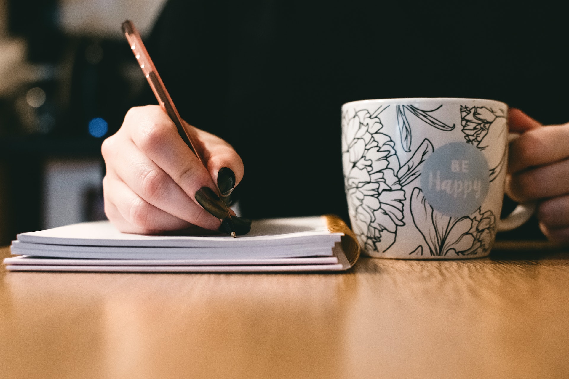 person writing in a journal holding a mug