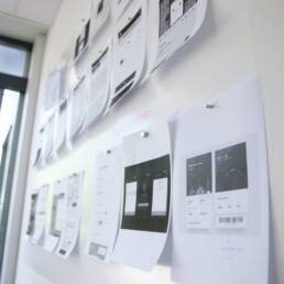 Printed out mobile design sketches are pinned to a wall.