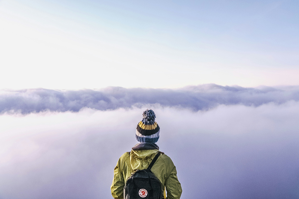 A traveler overlooks a cloudy overtop.