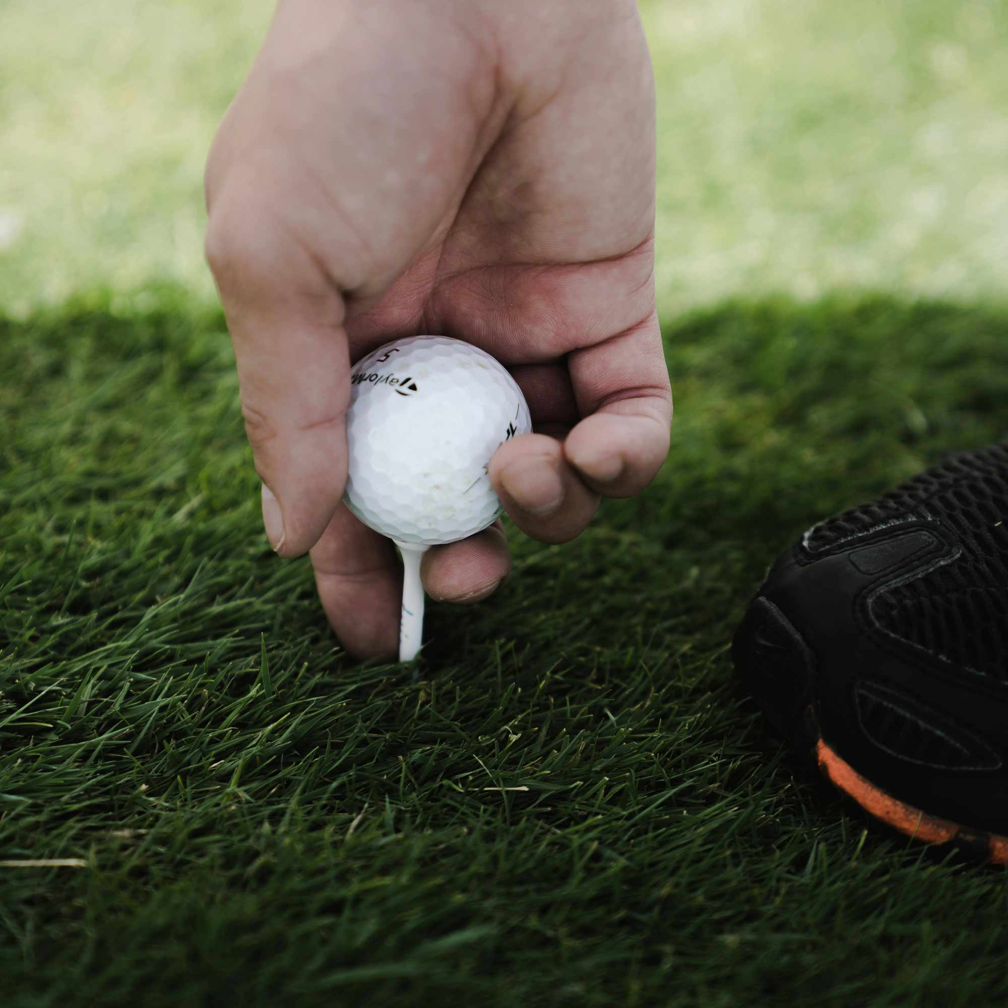 A hand holding a golf ball on the golf course.