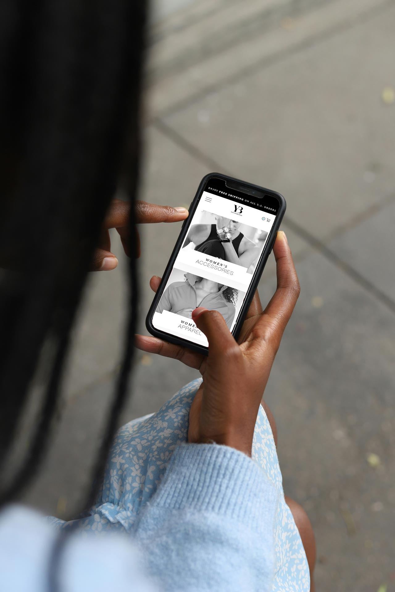 A person looks at a smart phone on a women's apparel and accessories web design page.