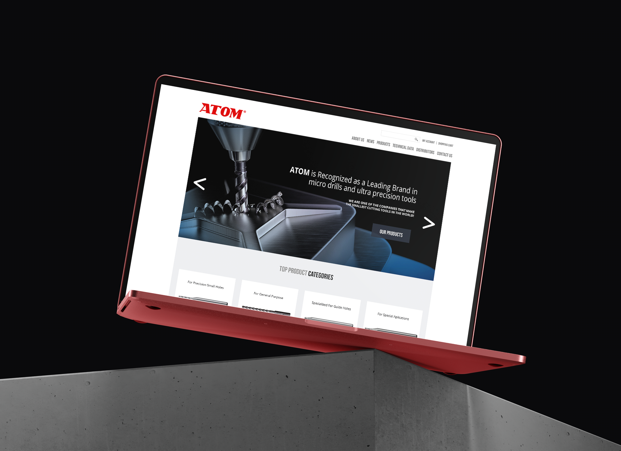 A red laptop on a metal desk displaying a home page for a manufacturing website.