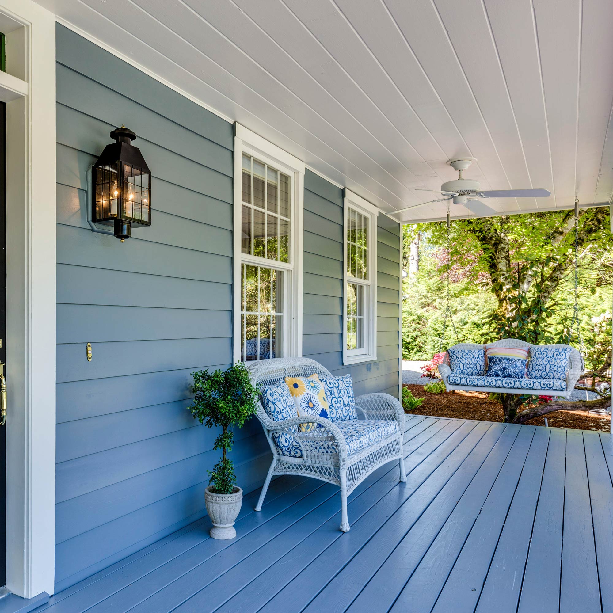 A blue front porch of a home with furniture outside.