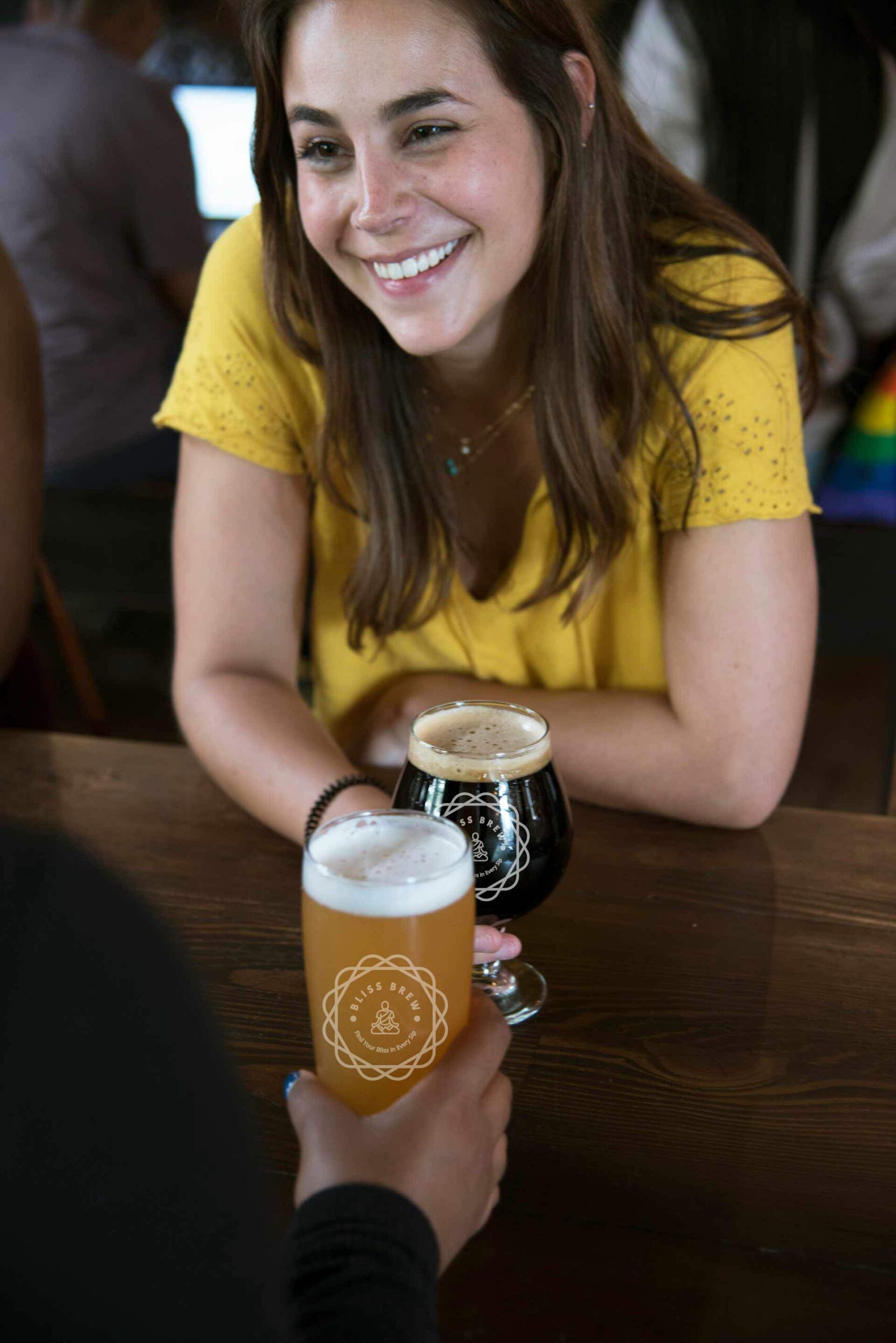 A person sitting at a table with a beer and smiling.