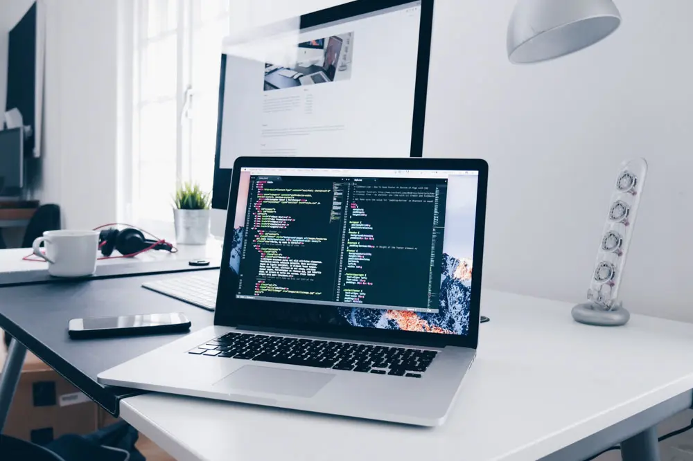 A laptop and desktop display with code on the screen.