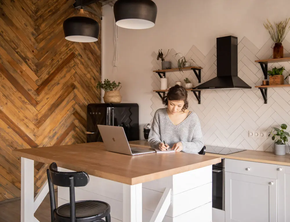 A person ideates on a notepad with a laptop open on the counter.