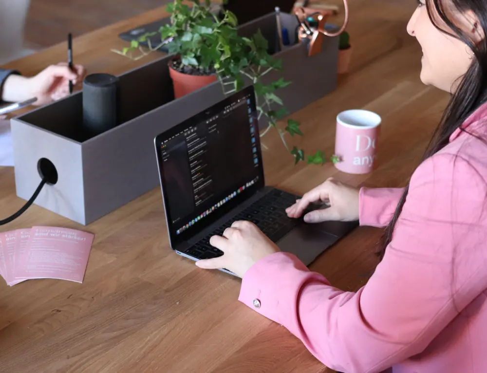 A web designer in pink uses a laptop.