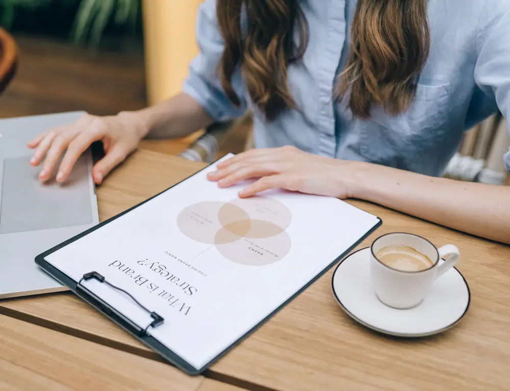 A person uses laptop while referencing a physical design.