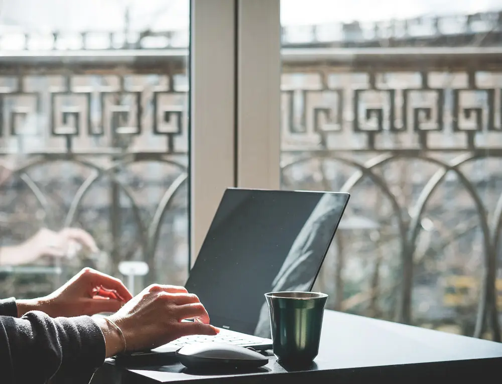 A person designs a website at a table by a window.