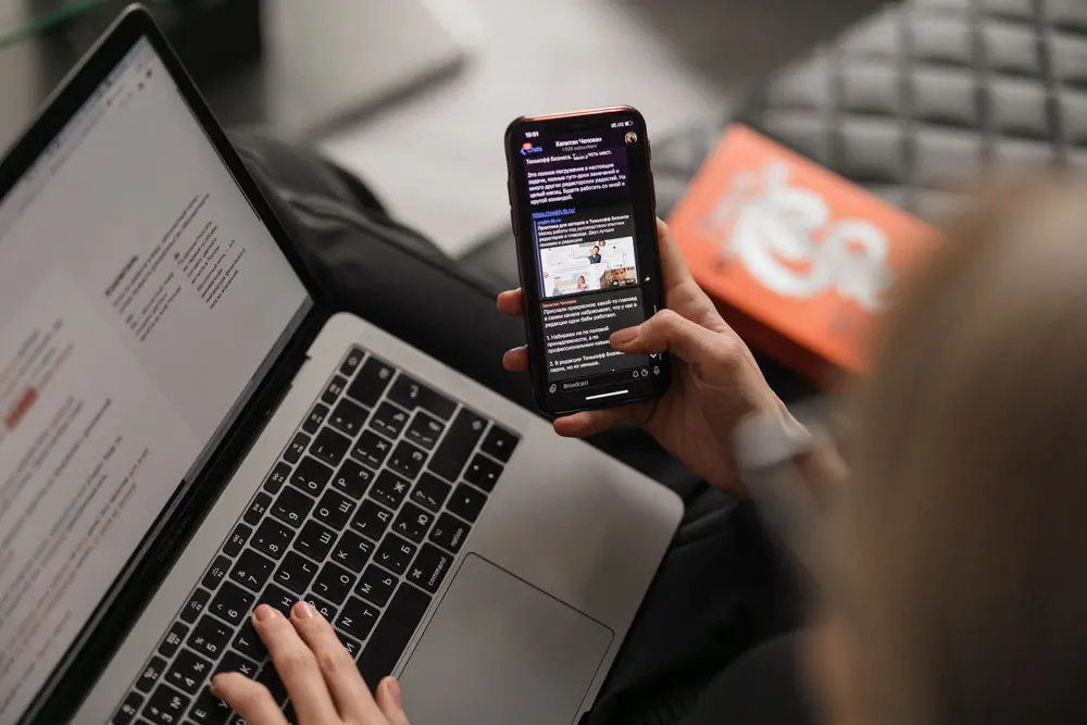 A person scrolls on their phone and their laptop at the same time.