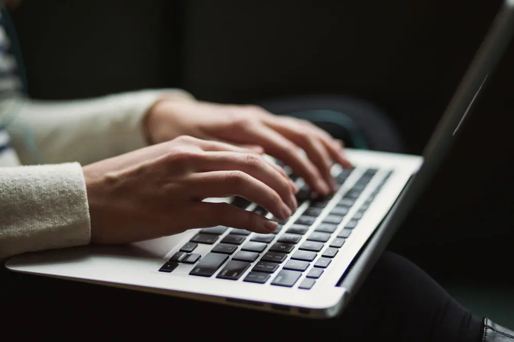 A person hands types on laptop in dimly lit room.