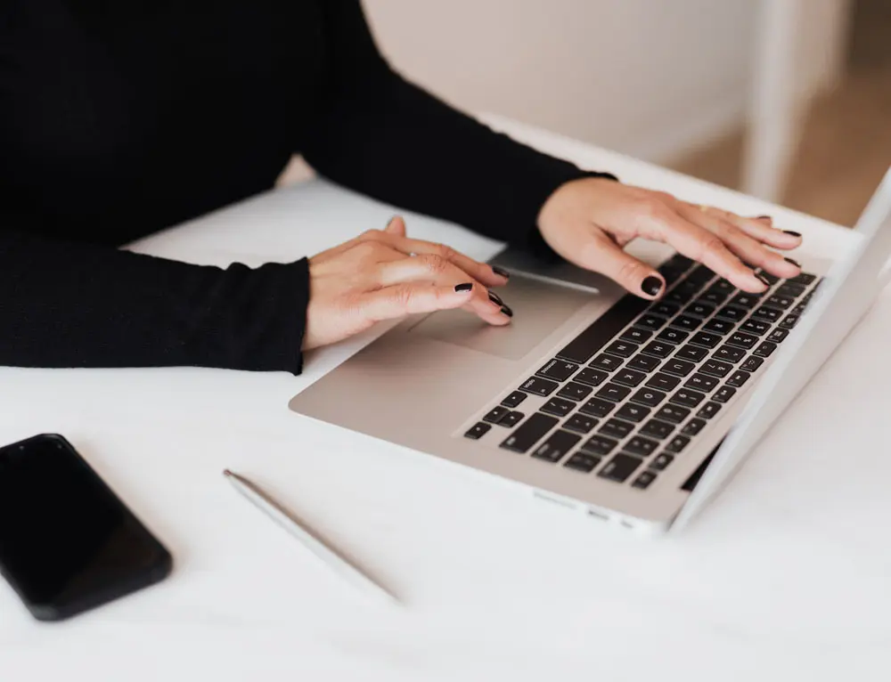 A user navigates an interface on their laptop device as an iPhone is placed beside the laptop.