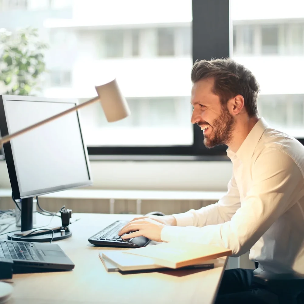 A person works on their office computer, smiling at the screen.