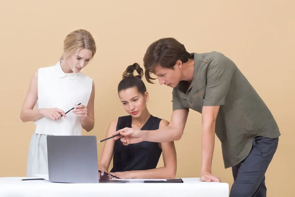 Three team members strategize web design on a single laptop.