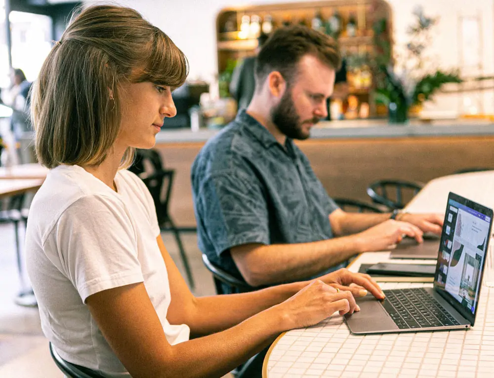 Two people sit and work on content strategy on their separate laptops.