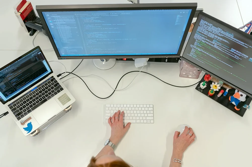 An bird eye view of a designer with three desktop screens writing code.