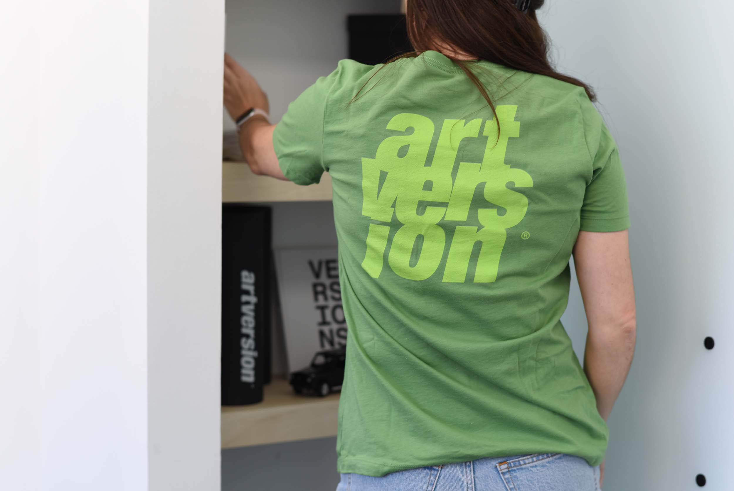 ArtVersion team member in green branded t-shirt reaching for items on a shelf filled with swag